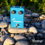 Turquoise Lemon & Ginger Takotavia octave-fuzz pedal with Volume and Boost controls, photographed outdoors on natural stones.