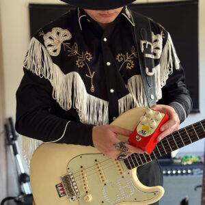 Blues guitarist Can Bayoglu holding a red RFO Electronics elMo’ overdrive pedal with his Strat-style guitar